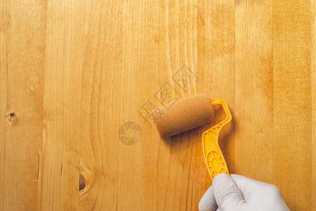 黄色木头手与油漆滚滚机 在木板上施用丙烯酸工具木头男人硬木维修男性黄色水基工艺家具背景