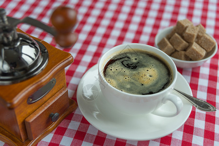 在白瓷杯子中的黑咖啡茶匙织物蔗糖飞碟咖啡研磨机桌布白色饮料背景图片