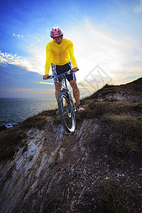 骑脚踏板年轻人骑着摩托脚踏板 在地面的沙丘上头盔娱乐日落男人自行车爬坡山地车悬崖日出男性背景