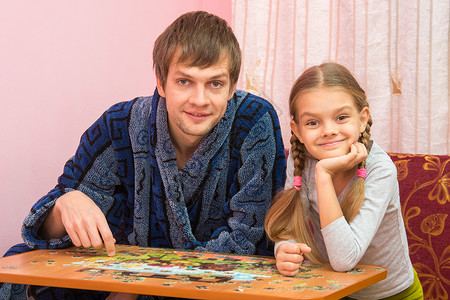 边框中的爸爸和女儿坐在桌子上收集拼图 看着桌边的壁画背景图片