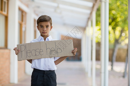 男学生持有的标牌上写着 请帮帮忙制服标语沟通门厅焦虑小学走廊学习学校男生背景图片