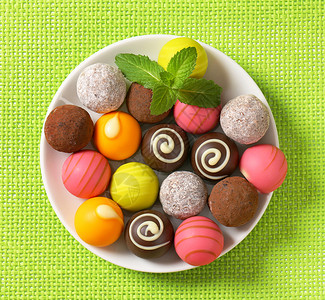 绿色杏仁巧克力球各种巧克力松露和菠萝甜点糖果绿色团体杏仁盘子奶糖水果粉色棕色背景
