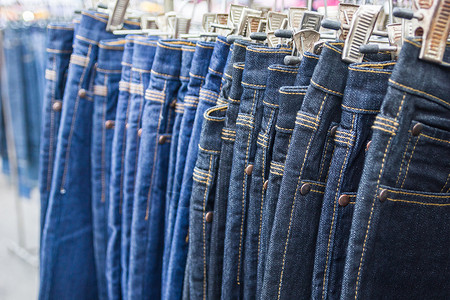 聚酯纤维很多不同的蓝色牛仔裤衣架服装销售展示织物架子市场陈列室店铺零售背景
