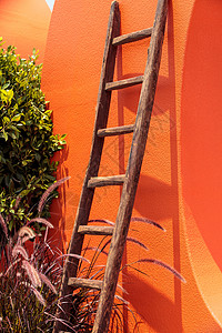 铁制木制梯子 对着明亮的橙色墙壁背景图片