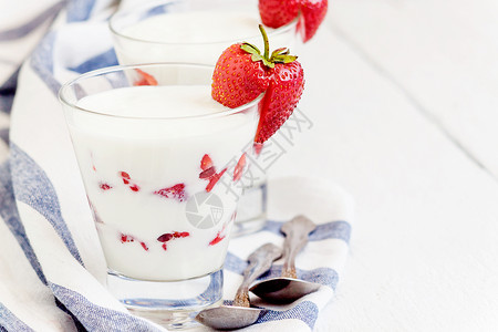 盛满草莓勺子甜甜酸奶和草莓层 在蓝色条纹的玻璃杯中食物牛奶奶制品饮食健康奶油毛巾水果桌子早餐背景