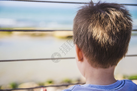 年轻男孩从金属围栏后面向远处的地平线看白色童年小男孩男性海洋男生栅栏青年希望孩子背景图片