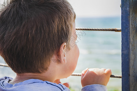 以色列游学网年轻男孩从金属围栏后面向远处的地平线看童年男生青年监狱男性希望海洋小男孩孩子栅栏背景