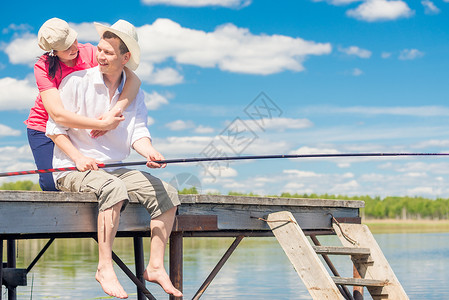 坐着钓鱼的女孩男人用钓鱼杆和他心爱的女人 在木头码头上背景