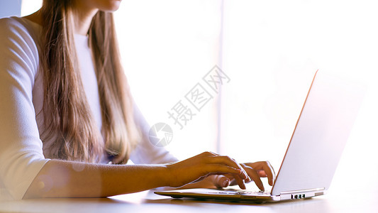 在大窗口前的笔记本电脑键盘上贴近女性手打字图像女孩耀斑窗户桌子学生工作衬衫太阳商业技术背景图片