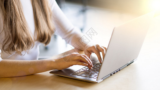 在大窗口前的笔记本电脑键盘上贴近女性手打字图像商业互联网衬衫技术耀斑购物人士学生太阳桌子背景图片