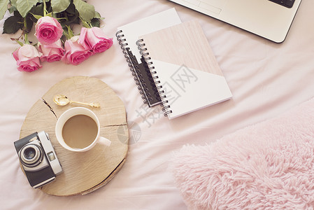 咖啡 躺在粉红色床单上的旧老式相机 周围有玫瑰 笔记本和膝上型电脑 平躺风格的自由时尚家居女性气质工作区背景图片