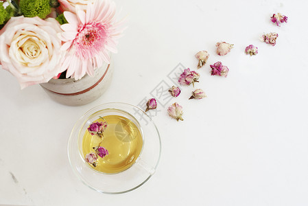 一杯含有干玫瑰的健康凉茶 浅色大理石桌上美丽的鲜花 顶视图 女性办公桌上的粉红玫瑰和非洲菊 博客生活方式背景图片