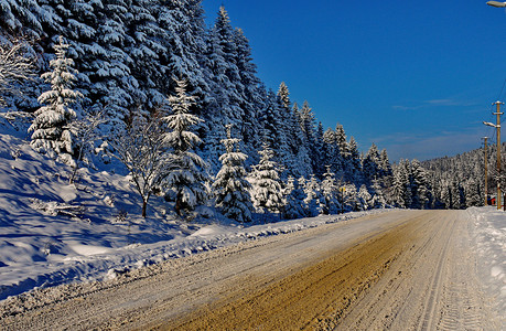 寒冷的冬天风景 在雪覆盖的斜坡上生长着一条沿着美丽的高山壁运行的滚动道路背景图片