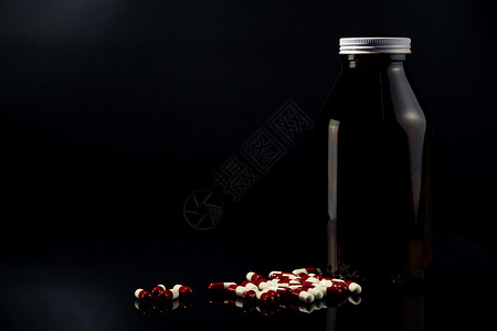 深色背景中的红色 白色抗菌胶囊药丸和琥珀色玻璃瓶 带有空白标签和文本复制空间 抗生素耐药与合理用药观念背景图片