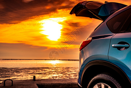 蓝色紧凑型SUV车 有运动和现代设计 停在日落时靠海的混凝土路面上;环保技术;海滩度假旅行和露天汽车背景图片