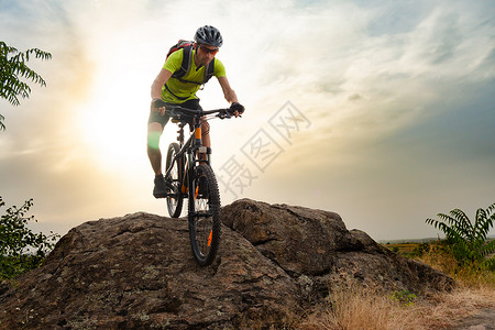 赛车手骑着自行车在日落日落的秋天岩轨上 极端运动和概念运动员车轮天空岩石蓝色耐力赛成人冒险头盔山地车背景