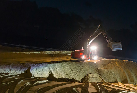 夜间工作挖掘挖土机 在海滩地面移动 以进行维修保养背景图片