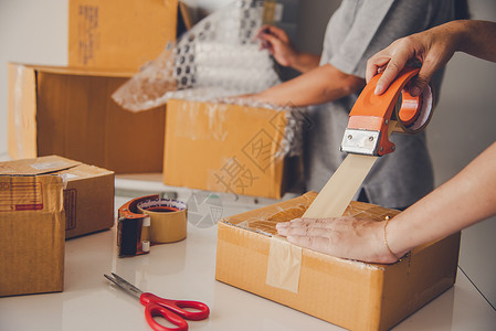 中小企业团队工作人员包装在棕色箱子中 将货物交付给客户家庭盒子男性生活磁带邮资开箱女性女士搬迁背景