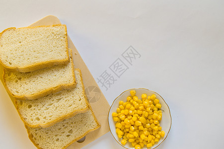 一盘熟玉米粒木板上的切片新鲜玉米面包片和桌子上的一盘玉米粒 白色隔离背景 顶视图 复制空间美食烘烤谷物草料粮食豆子食物面粉盘子正方形背景