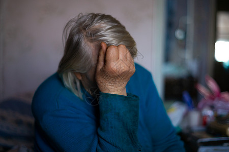 咳嗽老不好白头发老女人用手遮住她的脸 女人很悲伤 在村里生活悲惨 年老不好 低光照片背景