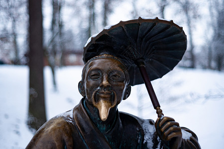 冬雪公园一个带雨伞的中国老人的铜质纪念碑 其背景模糊而封闭哲学家艺术石头文化历史青铜历史性旅行建筑学寺庙背景图片