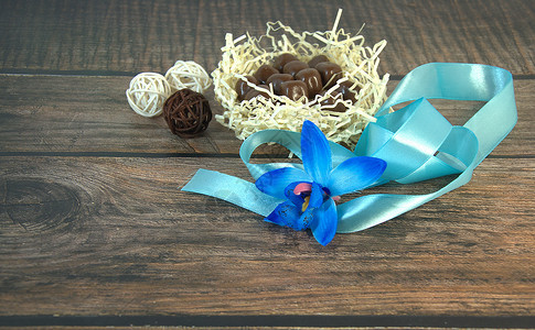 球兰花一窝干草和巧克力 蓝色丝带 蓝色兰花的花蕾和木桌上的装饰球植物群展示小样作品桌子横幅风格公园庆典背景