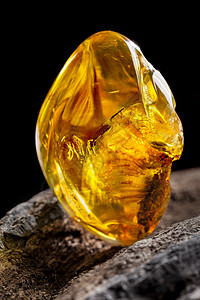 琥珀石天然琥珀 黄色透明的天然琥珀 在大片黑石头木头的一块上珠宝抛光宏观琥珀色宝石反射珠子化石蜂蜜材料背景