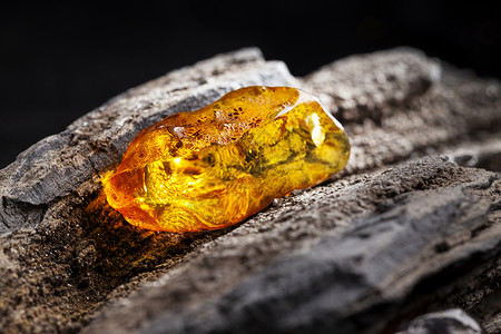 黑琥珀李天然琥珀 黄色透明的天然琥珀 在大片黑石头木头的一块上珠子蜂蜜宏观矿物琥珀色抛光反射珠宝材料烙印背景