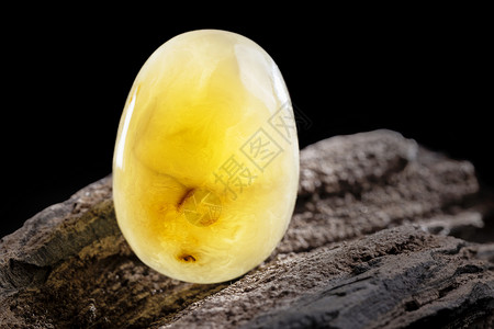 珠宝大片天然琥珀 黄色不透明的天然琥珀 在大片黑石头木头上矿物抛光琥珀色材料化石裂缝黄油反射分层太阳石背景