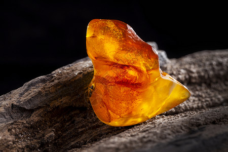 天然琥珀 一块黄色和红色半透明的天然琥珀 放在一块石头上宝石地质学裂缝晴天蜂蜜材料琥珀色太阳石矿物化石背景