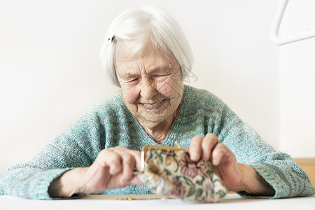 在家桌边坐着的96岁的老年妇女在支付帐单后对钱包中的养恤金储蓄感到欣慰 因为她很幸福孤独时间成人硬币女士女性贷款情感数数现金背景图片