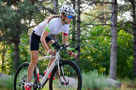 骑着锦鲤女人青年女赛车手骑着路自行车在夏日热火的森林中走免费道路 健康生活方式概念成人晴天速度冒险女性自由运动城市公园活动背景