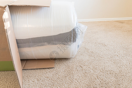 弹簧素材包在地毯地底背景上拆箱的 滚包装弹簧床垫贮存地面小地毯房子泡沫真空织物房间卧室纸板背景