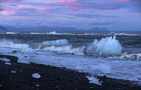 在黑沙滩上 日落时的蓝色冰山闪耀着背景图片