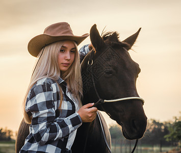年轻女孩穿着牛仔帽和一身带吊裤的格子衬衫村庄农场日落场地帽子天空头发衣服牧场蓝色背景图片