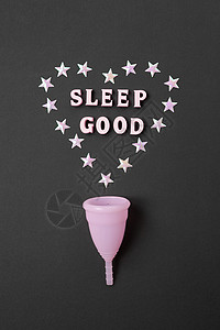 黑色背景中的粉红色月经杯 带有心形和文字“睡得好” 晚上使用杯子的概念可能性 零浪费 储蓄 极简主义 女性卫生用品 平躺 垂直的背景图片