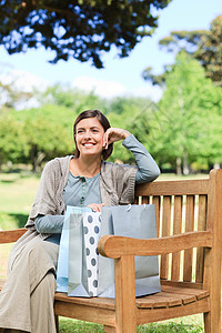 购物后的女人微笑花园女士女性闲暇绿色植物长椅幸福绿色公园背景图片