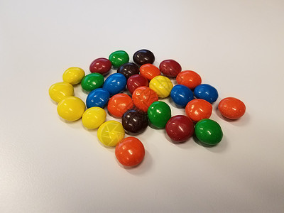 白色表面或桌子上的彩色巧克力糖果蓝色橙子食物绿色黄色背景图片