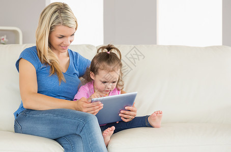 母亲和女儿在沙发上使用数字石板头发公寓闲暇金发浅色学习触摸屏家庭客厅童年背景图片