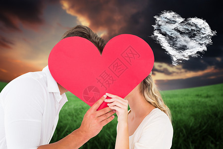 充满吸引力的年轻夫妇在大心脏后亲吻的复合形象情怀情人计算机情感金发公园纪念日天空金发女郎草原背景图片