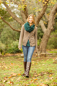 微笑的女人走在镜头前公园潮人环境寒冷女性夹克浅色绿地长发围巾背景图片