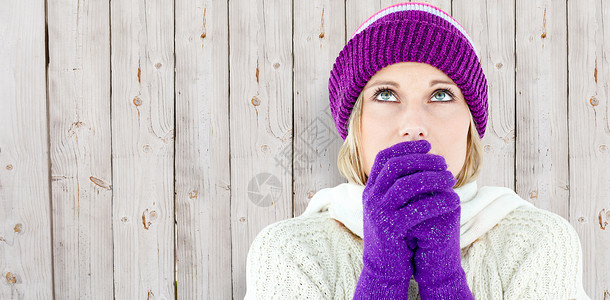 身戴手套往上看的年轻女性被冷冻的复合图像保暖女士羊毛衣物围巾栅栏帽子木头背景图片