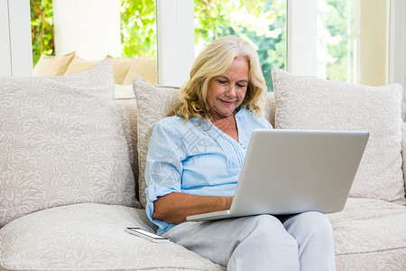 年长妇女在家中坐在沙发上时使用笔记本电脑背景图片