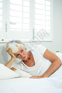 深思熟虑的老年妇女在床上放松枕头窗户服装老年人退休公寓女性休闲房子思维背景图片