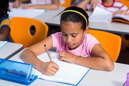 女孩在笔记本上写字发带女性同学们小学学校童年铅笔专注班级混血背景图片