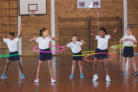 在篮球场玩hula hoop的学校儿童女性女学生孩子校服学生呼啦圈享受健身房大厅瞳孔背景图片