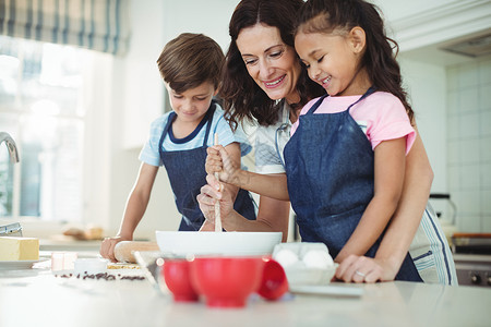 母亲和孩子在准备饼干时混合面团住所女性厨房快乐现实互动家庭男生女孩微笑背景图片