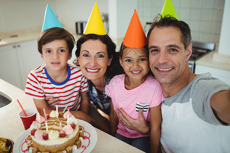 双色派对帽在庆祝生日时 快乐的一家人拿自拍回忆房子公寓技术女儿母亲父亲沟通派对孩子背景