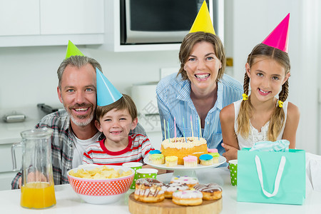 双色派对帽一起在厨房庆祝生日的笑脸家庭 在厨房里背景