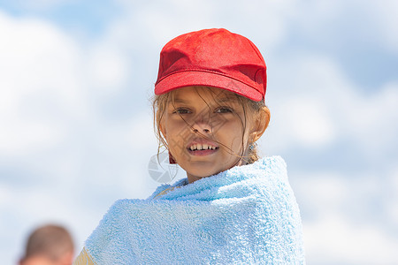 穿着红帽子的女孩的肖像 裹在毛巾上对着天空背景图片